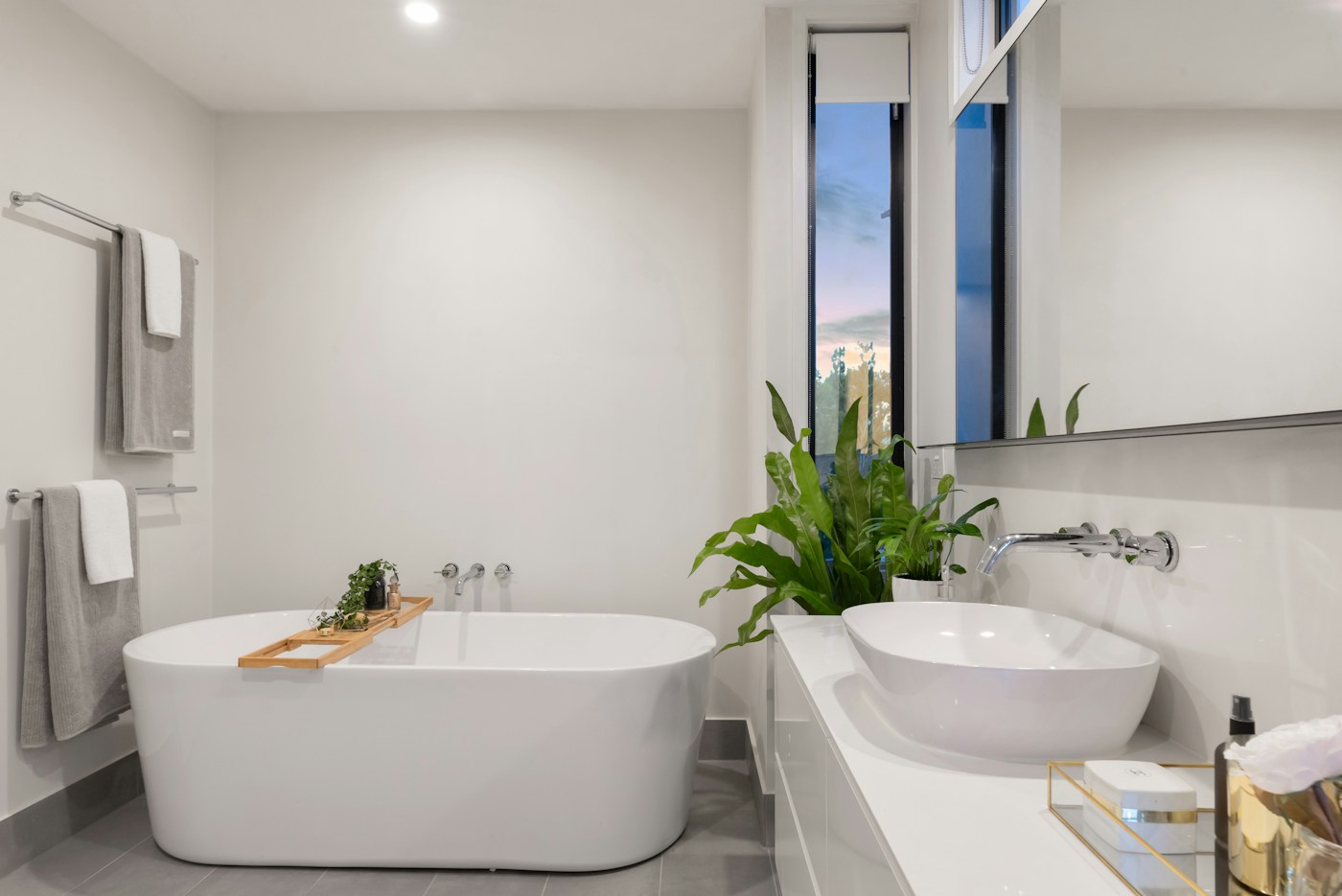 A bathroom with a freestanding tub, vessel sink and pale stone surfaces