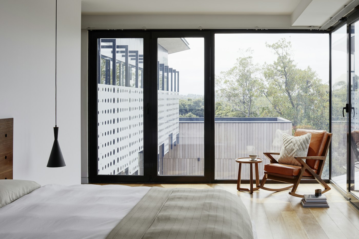 A bedroom with full-height windows, a leather chair and natural wood flooring